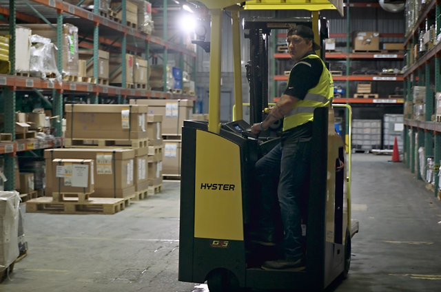 A worker operating a three-wheel stand forklift 